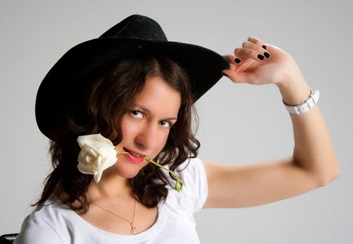 young woman in black hat with white rose in her mouth posing in studio