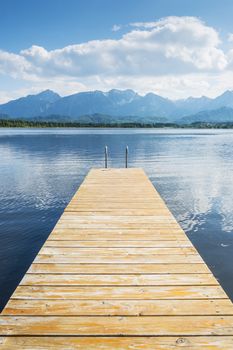 Jetty on the lake named Hopfensee with the Alps and blue sky