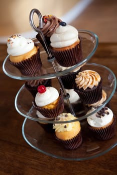 Tiered party serving tray with some decadent gourmet cupcakes frosted in a variety of flavors.