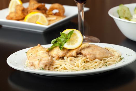 Chicken francaise or francese plated with pasta with salad and fried shrimp appetizer in the background.