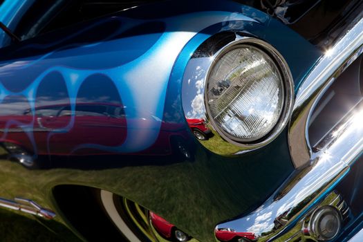 A closeup of the headlight and front bumper on a vintage car.