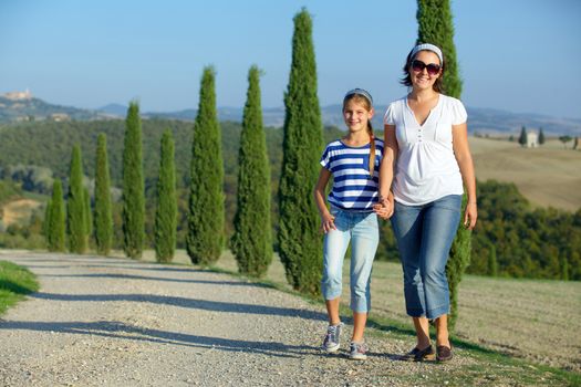 Happy mother with her daughter having fun on vacations in Tuscan against cypress alley background