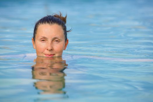 Smiling woman in bathing suit submerged in geothermal mineral pool. Iceland
