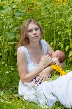 Young mother with the baby among blossoming sunflowers