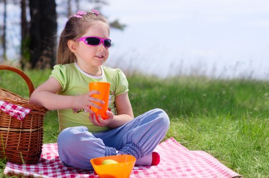 Little girl with picnic basket and plastic cup at lawn