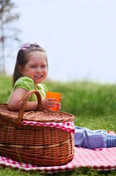 Little girl with picnic basket and plastic cup at lawn