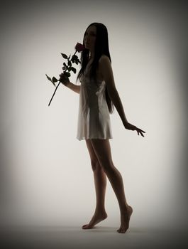 Silhouette of young girl with rose flower on gray background