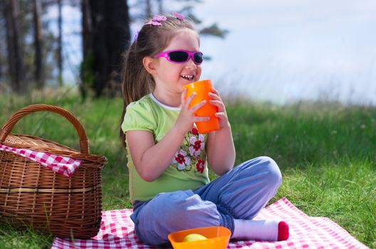 Little girl with plastic cup and picnic basket at forest