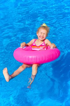 Funny little girl swims in a pool in an pink life preserver