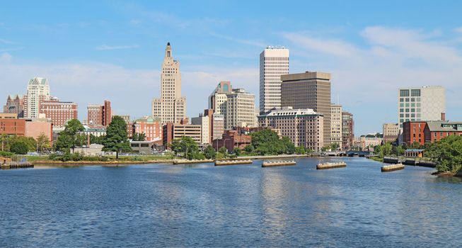 Panoramic view of the skyline of Providence, Rhode Island, from the far side of the Providence River against a blue sky and white clouds