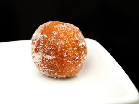 Donut ball, with sugar, on white plate towards black background