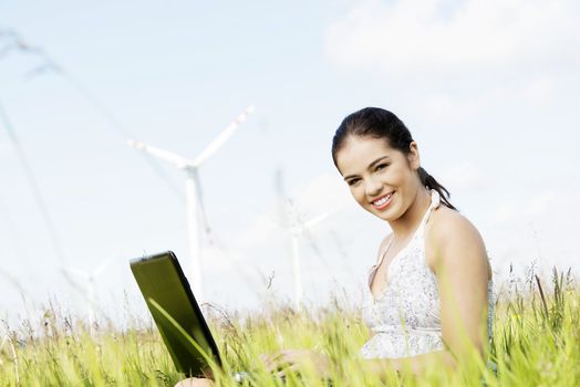 Teen girl with laptop computer next to wind turbine. Ecology - renewable energy concept.