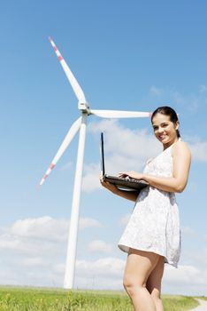 Teen girl with laptop computer next to wind turbine. Ecology - renewable energy concept.