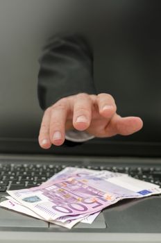 Male hand coming out of computer screen and stealing ones money. Concept of internet theft.
