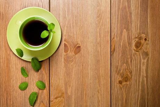 Tea mint in green cup with mint leaves on wooden table background. Top view