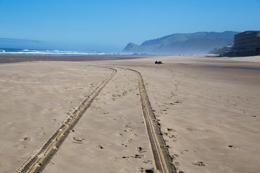 A set of tire mark tracks goes down the beach after a safety vehicle drove through.