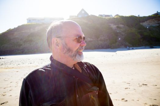 An attractive father faces to his right while the photographer take a portrait in color while shooting into the sunlight to create a unique backlit image of this man on the beach.