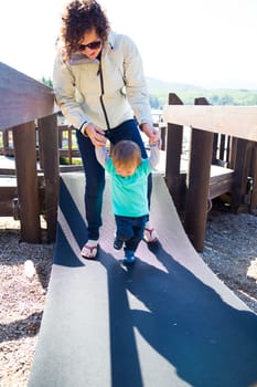A mom and her son cross an unstable bridge at a playground together.