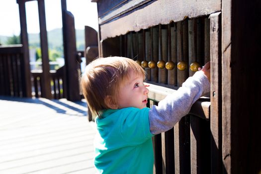 A young boy plays some sort of bells musical instrument at the playground in a park outdoors.