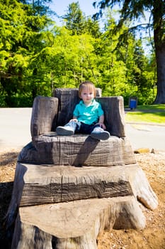 A cute young boy sits on a stump carved into a seat at a park outdoors for this cute and simple portrait.