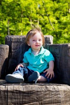 A cute young boy sits on a stump carved into a seat at a park outdoors for this cute and simple portrait.