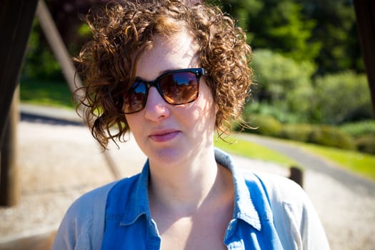 This beautiful attractive woman wears sunglasses outdoors at a park for a simple portrait of a female person.