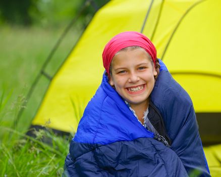 Young girl in a sleeping bag near tent in camping on the nature