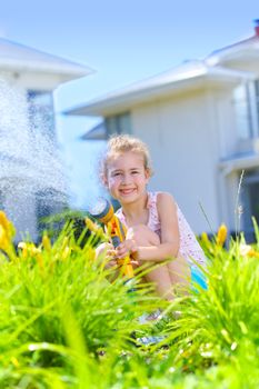 Little gardener girl watering flowers on the lawn near cottage. Vertical view