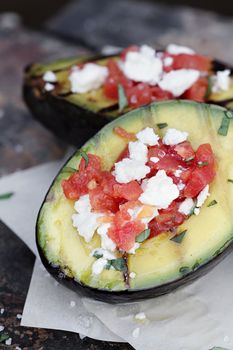 Grilled avocados filled with diced tomatoes and feta cheese and garnished with olive oil and freshly chopped parsley. 
