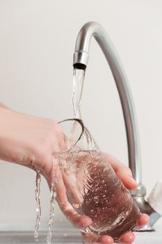 Human hand washing dish or pouring glass with fresh drink water at kitchen faucet