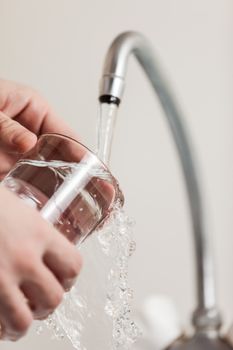 Human hand holding glass pouring fresh drink water at kitchen faucet