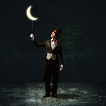 magician in top hat and tie, holding a glowing moon on a string