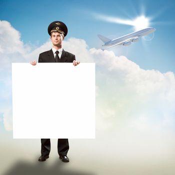 pilot in the form of holding an empty billboard on the background of sky and flying plane, place for text