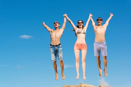 a group of young friends jumping on a background of blue sky, having fun