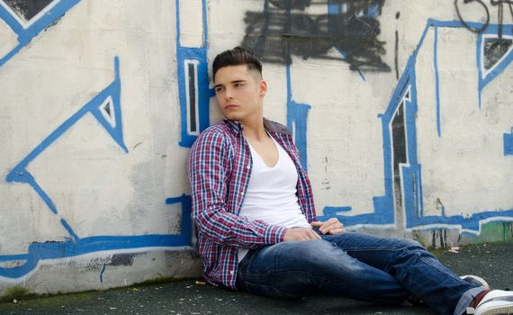 Handsome young man sitting on ground against colorful graffiti covered wall