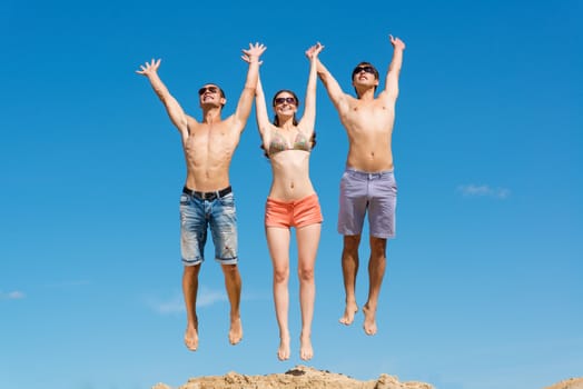 a group of young friends jumping on a background of blue sky, having fun