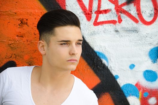 Handsome young man against colorful graffiti covered wall