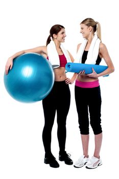Two girls communicating in gym. One holding exercise ball and other one blue mat