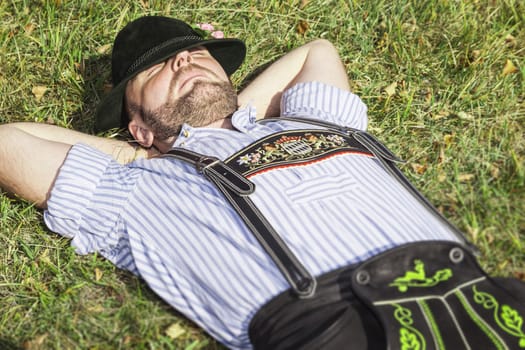 An image of a traditional bavarian man relaxing in the grass