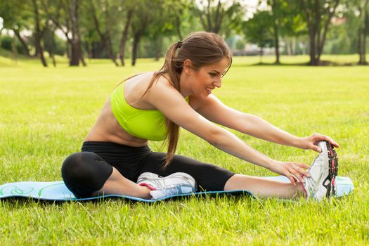 Beautiful young caucasian woman in fitness wear exercising on a grass