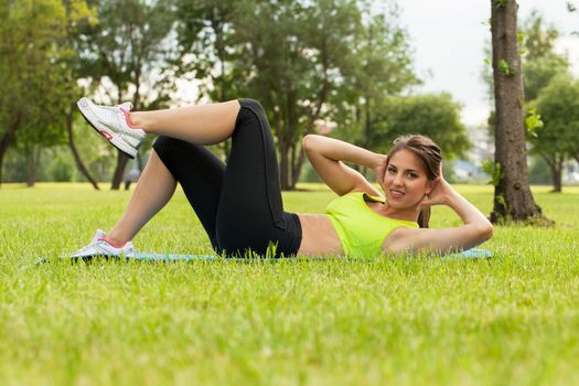 Beautiful young caucasian woman in fitness wear exercising on a grass