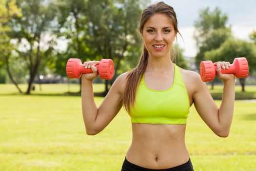 Young caucasian woman working out with dumbbells in a park