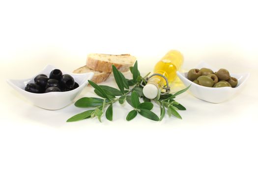 Bottle of olive oil with olives, crispy baguette and olive branch on a bright background