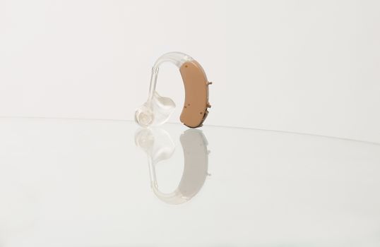 Single behind-the-ear hearing aid device with ear mould and tubing on a reflecting glass surface.