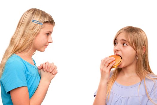 Girl begging for a piece of hamburger with folded hands to another girl. Isolated on white.