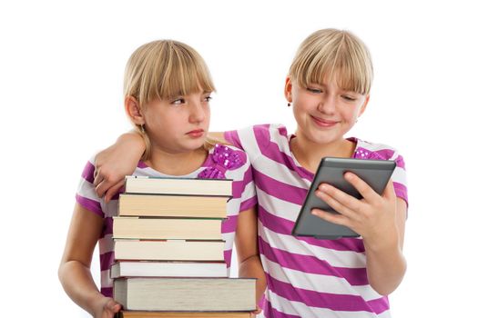 Books vs ebook reader - Two girls demonstrating the difference. One of them holding lots of books while anoter reading and ebook reader and smiling.