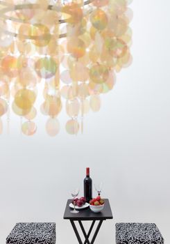 Bottle of red wine on a table, in a room decorated with beautiful chandelier. Focus on the table.