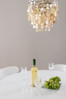 Decorative chandelier and bottle of white wine with grapes on the table.