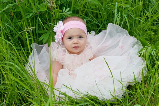 little girl in an elegant dress sits on a grass