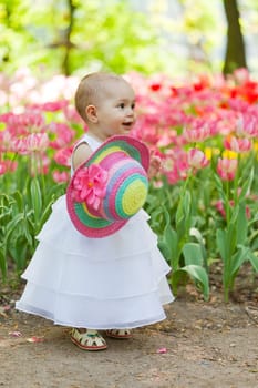 baby in an elegant dress near blossoming tulips